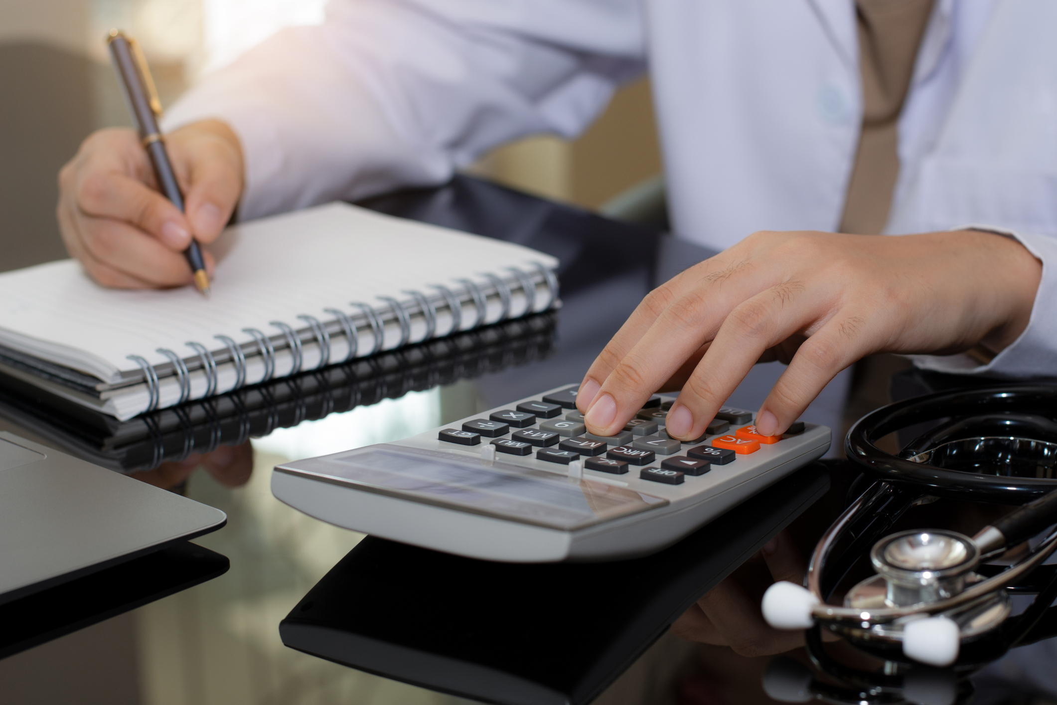 Close up doctor using calculator and work on laptop computer at office. Medical healthcare costs and fees concept.
